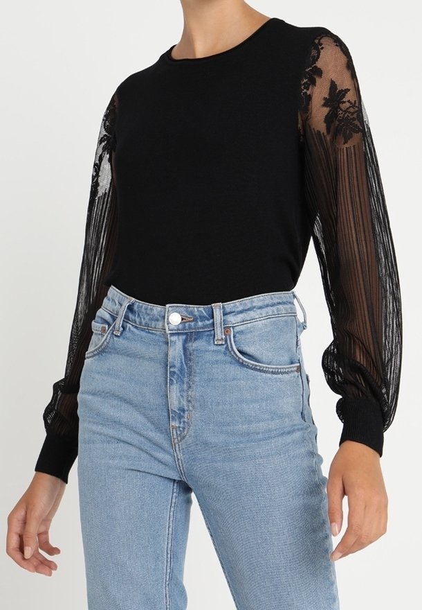 Zwart gebreid top met doorschijnende, gestreepte kanten mouwen met bloemdetails, gecombineerd met lichtblauwe high-waisted denim jeans.