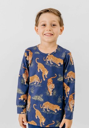 Lächelnder Junge mit kurzen Haaren, der ein marineblaues Langarmshirt mit orangefarbenen Tigern und Leoparden in verschiedenen Posen trägt.