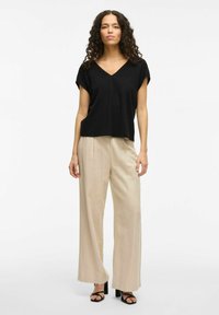 Top nero a maniche corte con scollo a V, abbinato a pantaloni beige a gamba larga. L'outfit presenta una vestibilità rilassata e una texture del tessuto morbida.