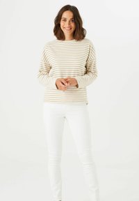 Blusa de manga larga a rayas en crema y beige claro, con un corte relajado y escote redondo, combinada con unos jeans blancos ajustados.