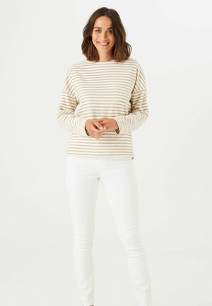 Gestreiftes Langarmshirt in Creme und hellbeige, mit lockerer Passform und rundem Ausschnitt, kombiniert mit engen weißen Jeans.