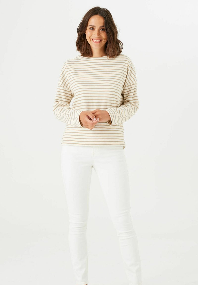Blusa de manga larga a rayas en crema y beige claro, con un corte relajado y escote redondo, combinada con unos jeans blancos ajustados.