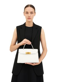 Borsa a spalla in pelle bianca con chiusura dorata, forma strutturata, manico corto e texture liscia, tenuta da un modello in un completo nero.
