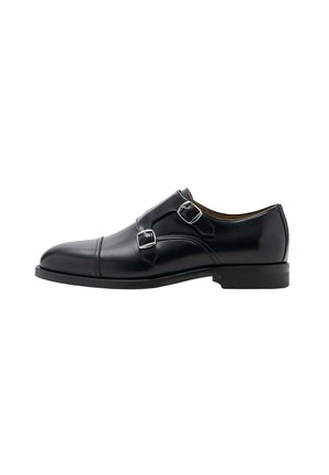 Zwarte leren monkstrap herenschoen met dubbele gespen en lage hak, gezien vanaf de buitenkant tegen een witte achtergrond.