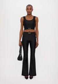 Top corto nero e pantaloni svasati realizzati in un tessuto liscio, con dettagli in hardware dorato. Il modello tiene una piccola borsa nera.