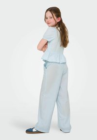 Top peplum bleu clair à manches courtes, associé à un pantalon large. Ses caractéristiques notables incluent un tissu doux et des poches latérales.
