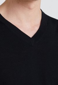 Pullover nero a scollo a V realizzato in un tessuto lavorato a maglia, con una finitura liscia e una vestibilità aderente attorno al collo e alle spalle.