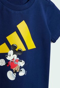 Mörkblå bomull t-shirt med en bild av Mickey Mouse i röd skjorta och beige shorts, tillsammans med gula diagonala ränder.