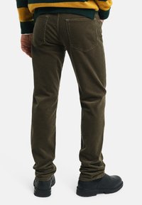 Oliwkowe spodnie o slim fit, wykonane z teksturowanej tkaniny, z dwiema tylnymi kieszeniami i zamkniętym dołem, w połączeniu z czarnymi botkami za kostkę.