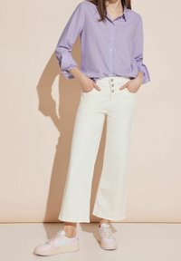 Vita vida byxor med hög midja och femknäppt stängning, kombinerat med en lavendel- och vitrandig skjorta med knappar och rosa sneakers.