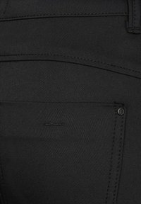 Svart denimtyg med en slät textur. Har en bakficka med subtil sömnad och en liten metallnitaraccent nära sömmen.