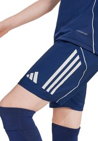 Marineblauwe sportshorts van vochtafvoerend materiaal, met witte Adidas-strepen en een gestructureerd ontwerp met een elastische tailleband.