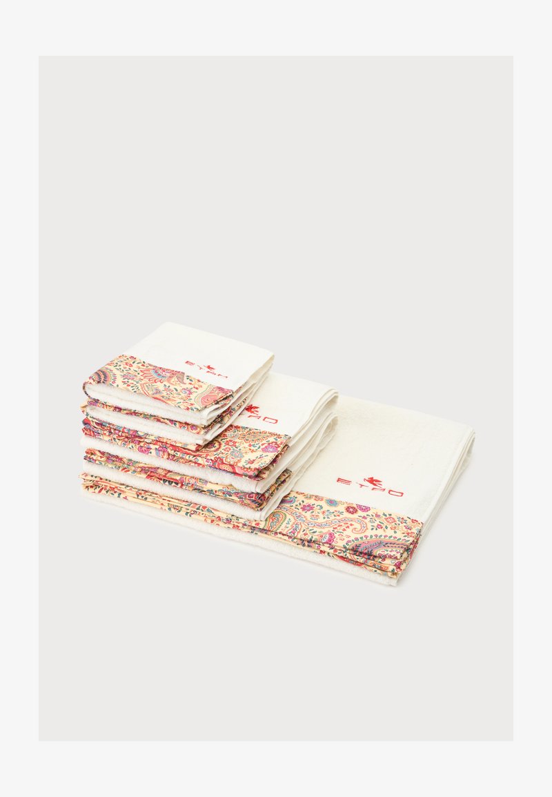 Pile de serviettes blanches avec des bords à motifs floraux et cachemire colorés et texte brodé en rouge sur un fond uni.