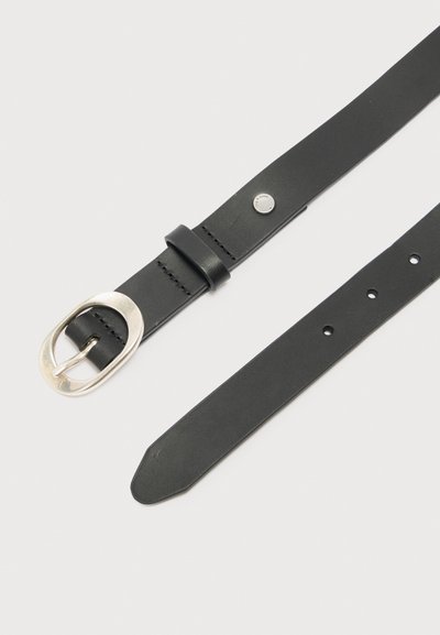 Μαύρη δερμάτινη ζώνη με οβάλ ασημένια πόρπη, πέντε τρύπες για ρύθμιση και μικρή μεταλλική λεπτομέρεια με καρφί σε ανοιχτό φόντο.