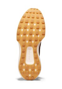 Brun skosula med en texturerad gul gummigriff, vit mellansula och hexagonalt mönster för grepp. Varumärket är synligt.