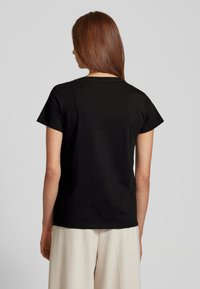 T-shirt nera in cotone con maniche corte, colletto tondo e una texture liscia. Design minimalista senza motivi o accenti aggiuntivi.