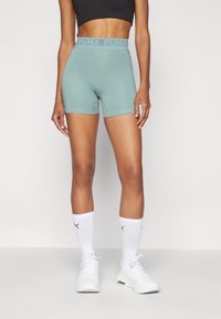 Shorts sportivi verde chiaro con una cintura spessa e a coste che presenta il logo "PUMA", abbinati a calze bianche a metà polpaccio e scarpe da ginnastica bianche.