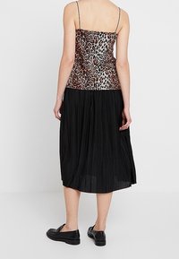 Black pleated skirt with a leopard print bodice and thin shoulder straps, worn with black slip-on shoes. Plain light background.