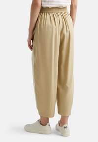 Béžové, volně střižené kalhoty s nařaseným pasem, bočními kapsami a lehkou tkaninou, kombinované s bílými teniskami.