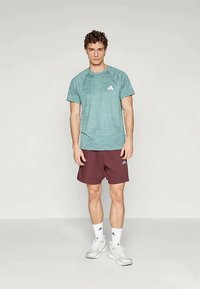 Türkiissinine spordisärk lühikeste varrukatega ja triibuline muster, kombineeritud maroonide lühikesed püksid, kandes valgeid sokke ja jalanõusid.