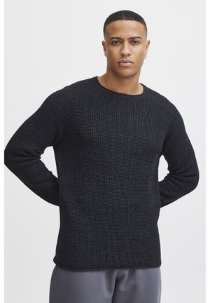 Black knitted sweater with a textured pattern, round neckline, and long sleeves, paired with gray pants.