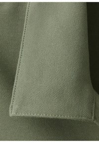 Primer plano de tela texturizada de color verde claro con costuras visibles en un borde doblado.