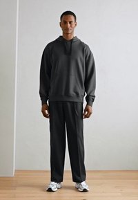 Grijze hoodie met een voorzak, gecombineerd met bijpassende grijze broek. Model draagt witte sneakers. Eenvoudig, ontspannen pasvorm ontwerp.