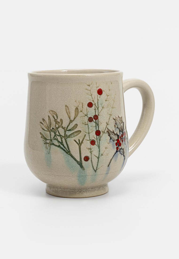 Keramiktasse mit einer strukturierten, beigen Oberfläche, verziert mit grünen botanischen Illustrationen und roten Beeren. Gekrümmter, stabiler Boden und Griff.