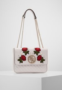 Bílá prošívaná kabelka se zlatými doplňky, s vyšitými červenými růžemi a zelenými listy, zdobená dekorativními hroty na přední straně.
