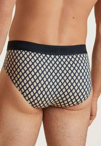 Marineblauwe onderbroek met een patroon van een gestructureerde stof. Heeft een geometrisch ruitpatroon in crème en lichtgroen. Het elastische waistband is zichtbaar.