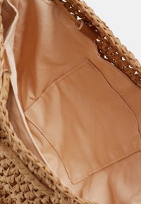 Sac en fibres naturelles tissées avec une doublure intérieure beige clair et une petite poche intérieure, doté d'une ouverture supérieure et d'une surface texturée.