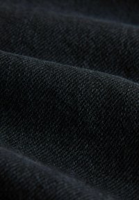 Tmavý denimový materiál s hladkou strukturou, který ukazuje diagonální vzor a jemné variace v odstínech, zdůrazňující hloubku a bohatost.