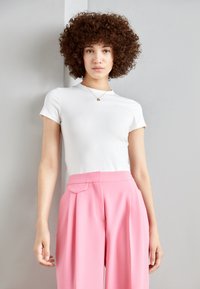 White short-sleeve top paired with high-waisted pink wide-leg trousers. Smooth fabric, casual fit, minimalistic design, subtle neckline detail.