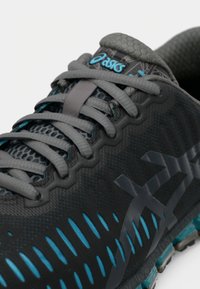 Gros plan d’une chaussure de course Asics noire et bleue avec des lacets gris, une tige en mesh et une semelle texturée.