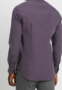 Langärmeliges Hemd in dunklem Lila mit kleinem weißem geometrischem Muster. Verfügt über einen Hemdkragen und geknöpfte Manschetten. Glatte Stoffstruktur.