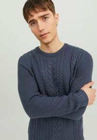 Marineblå strikket sweater med strukturerede mønstre, herunder kabelstrik. Har en rund halsudskæring og ribbede manchetter.