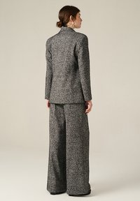 Completo grigio testurizzato con giacca aderente e pantaloni a gamba larga. Il tessuto presenta un motivo sfumato, offrendo una silhouette strutturata.
