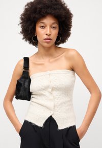 Top sem alças em tricô off-white com um padrão texturizado, botões frontais e uma bainha desfiada. Combinado com uma pequena bolsa preta de ombro.