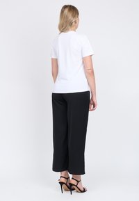 Hvid kortærmet t-shirt med rund halsudskæring, parret med sorte vide bukser og sorte højhælede sandaler. Enkel, afslappet pasform.