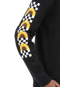 Sudadera negra de manga larga con tres girasoles amarillos y un patrón de tablero de ajedrez en blanco y negro en la manga derecha.