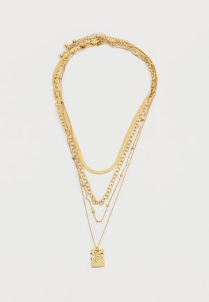 Conjunto de collares de oro en capas con estilos de cadena variados y un colgante rectangular texturizado en la cadena más larga, sobre un fondo blanco.