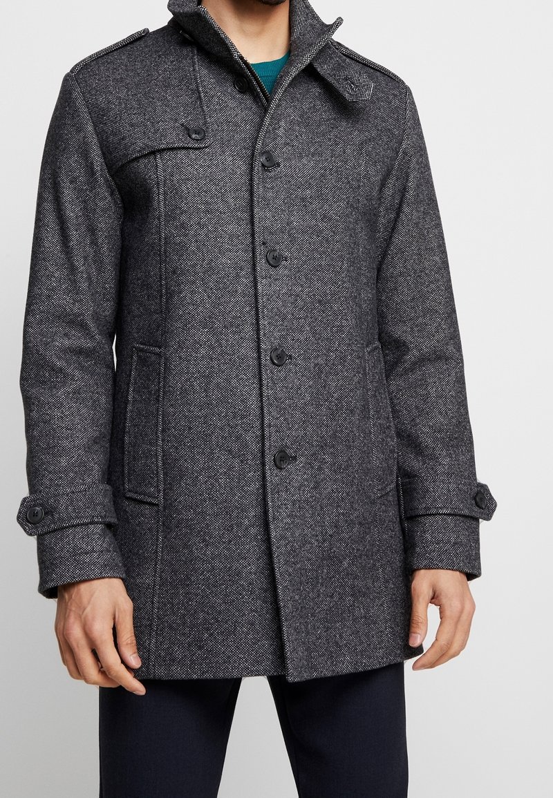 Mörkgrå ullkappa med en texturerad yta, med hög krage, knappstängning, sidofickor och justerbara ärmslut.