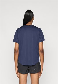 Σκούρο μπλε κοντομάνικο μπλουζάκι με στρογγυλή λαιμόκοψη, που έχει ελαφρώς μακρύτερο πίσω στρίφωμα, φορεμένο με μαύρες βερμούδες.