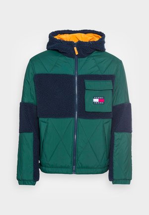 Zielona pikowana kurtka z granatowymi panelami z polaru, kapturem podszytym pomarańczowym materiałem, przednim zamkiem błyskawicznym, kieszenią z klapką oraz logo Tommy Jeans na kieszeni na piersi.