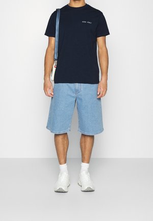 T-shirt in cotone blu navy con testo "GOOD VIBES", abbinato a pantaloncini in denim azzurri e sneakers bianche con suole testurizzate.