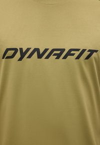 Ύφασμα ελιάς με έντονο μαύρο κείμενο «DYNAFIT» τυπωμένο οριζόντια στο κέντρο.