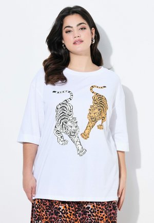 T-shirt bianco con illustrazioni di tigri nere e arancioni. Maniche corte, vestibilità comoda, realizzato in cotone morbido. Abbinato a una gonna a fantasia.