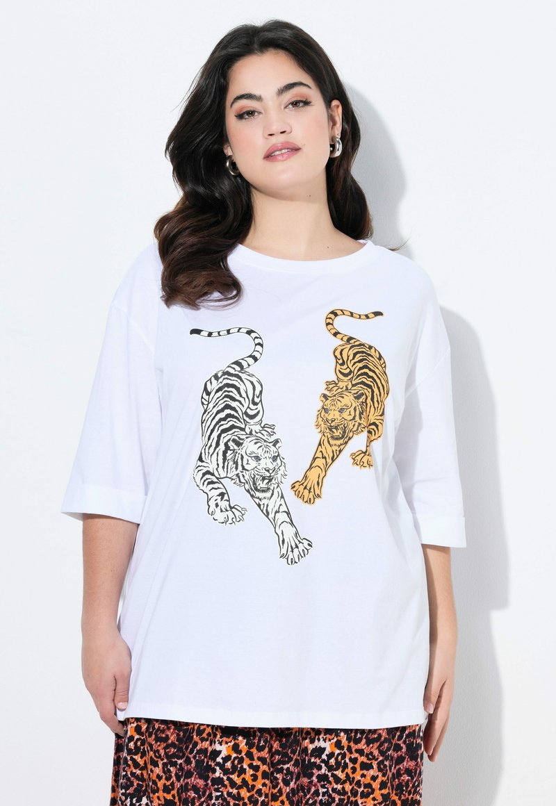 T-shirt blanc avec des illustrations de tigres noirs et oranges. Manches courtes, coupe décontractée, en coton doux. Associé à une jupe à motifs.