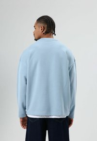 Lichtblauwe oversized sweatshirt van zacht stof, met een ronde hals en verzonken schouders. Gecombineerd met donkerblauwe jeans.