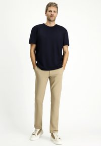 T-shirt navy a maniche corte, pantaloni beige slim-fit e sneakers bianchi. La t-shirt ha un collo tondo, una texture liscia e una vestibilità rilassata.